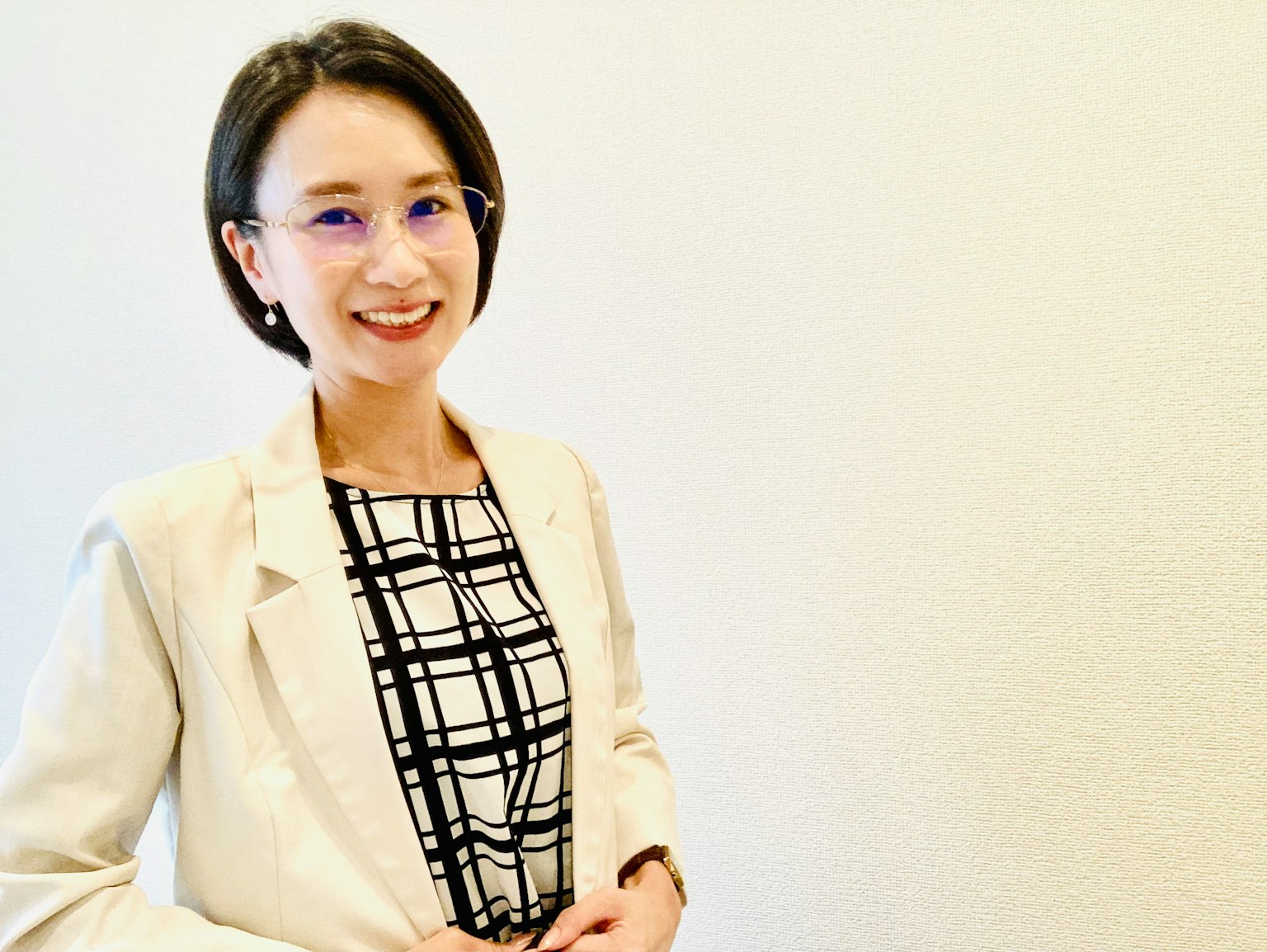 Eine Frau lächelt vor einem weißen Hintergrund Sie trägt einen Anzug und eine Brille