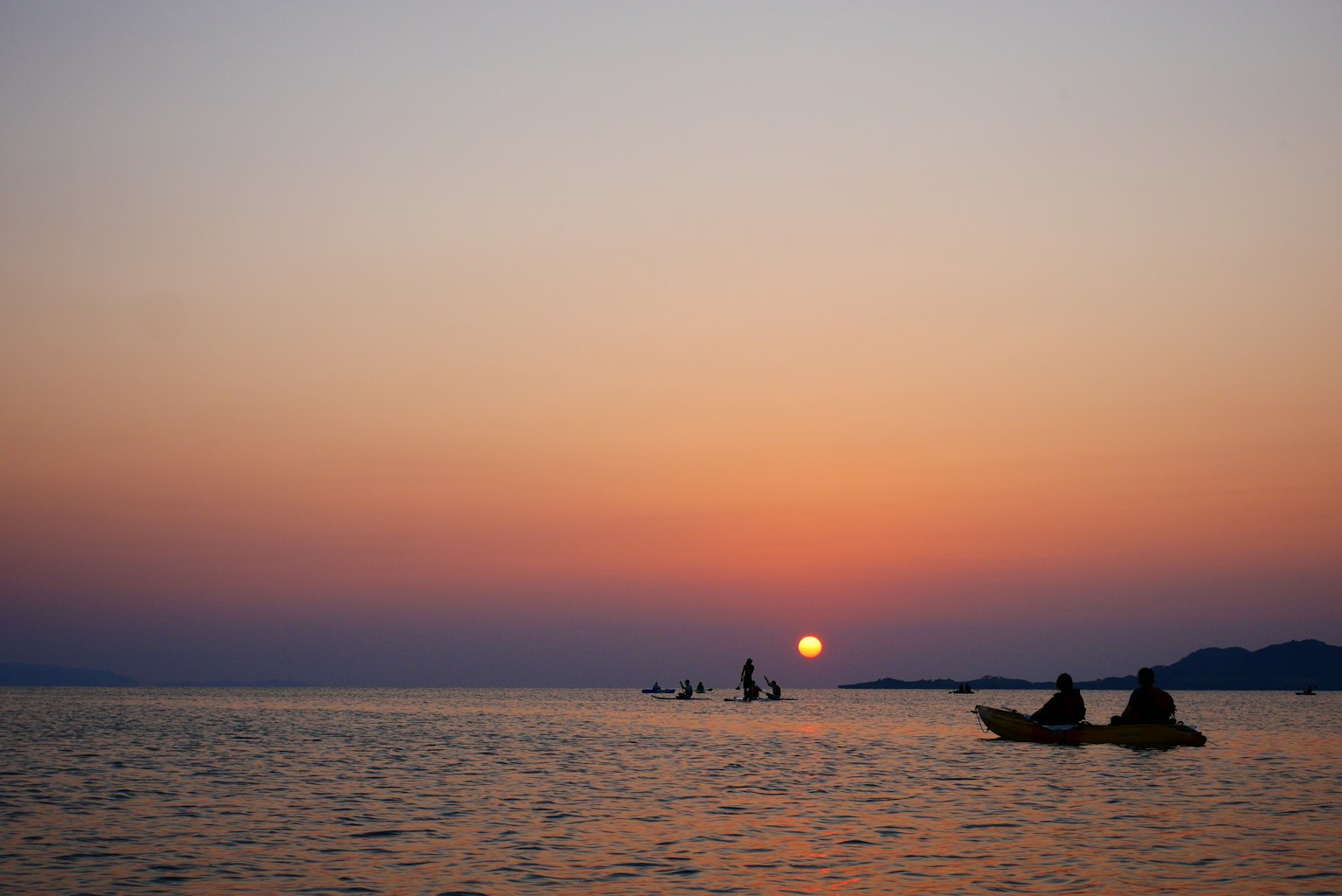 夕阳背景下在平静海面上划皮艇的人们