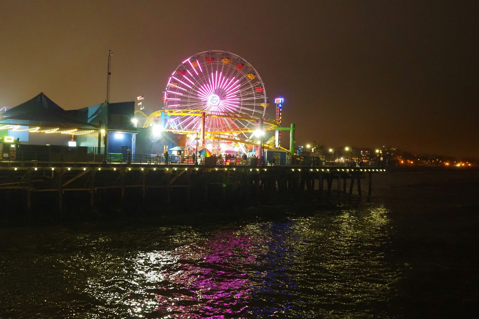 Vue nocturne d'une jetée avec une grande roue colorée se reflétant sur l'eau
