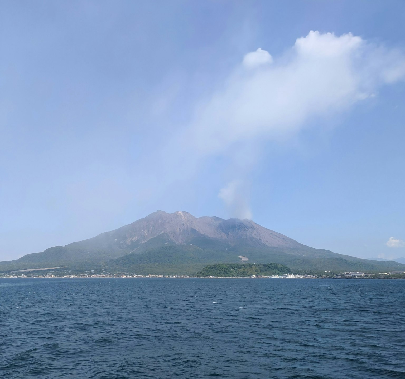 Vista del volcán Sakurajima con humo elevándose sobre el mar azul