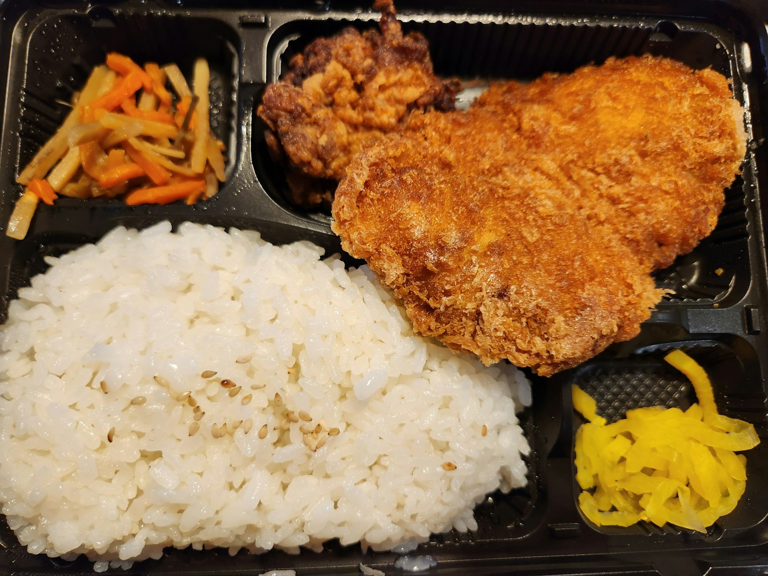 一個便當盒，裡面有炸雞米飯醃製的蔬菜和色彩豐富的配菜