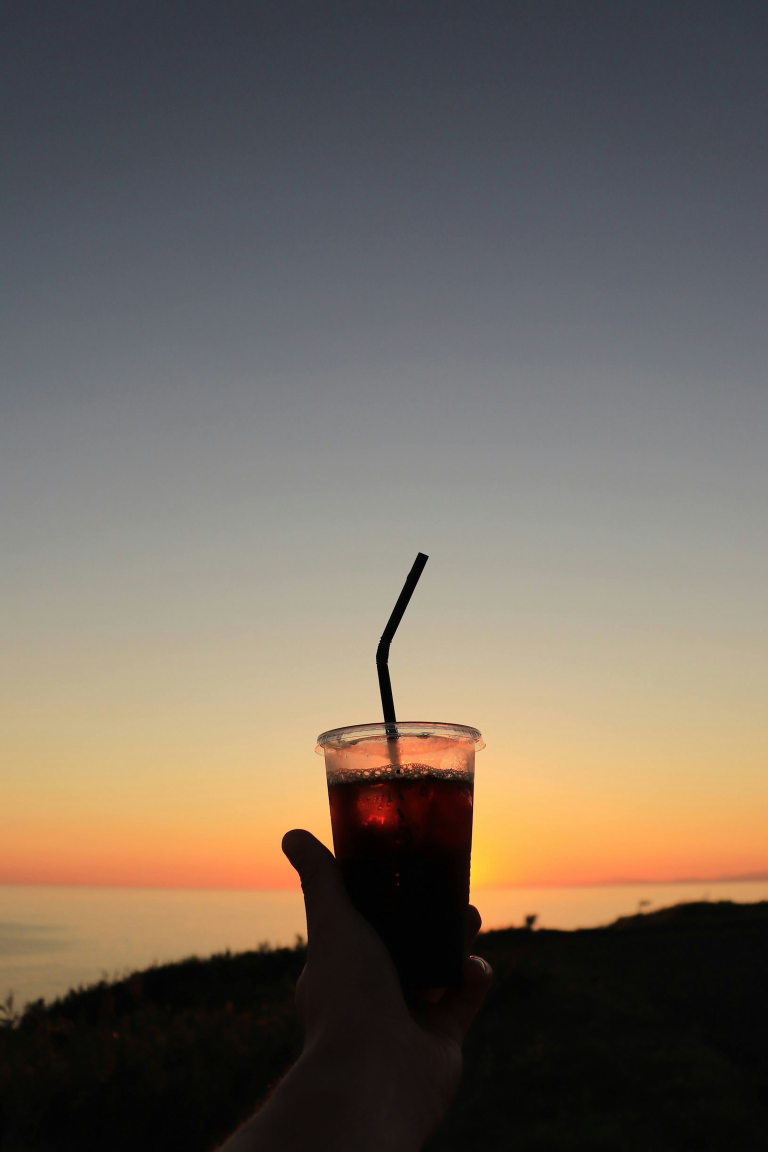 Getränkebecher, der vor einem bunten Sonnenuntergangshimmel gehalten wird