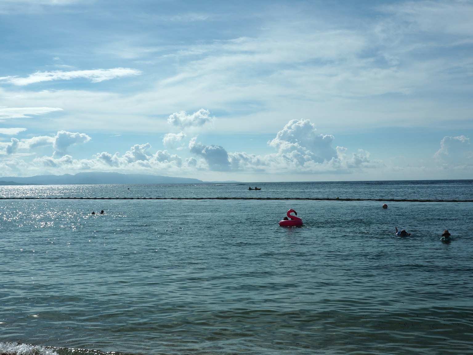 Eine malerische Aussicht auf ein blaues Meer mit weißen Wolken und einem schwimmenden roten Boot