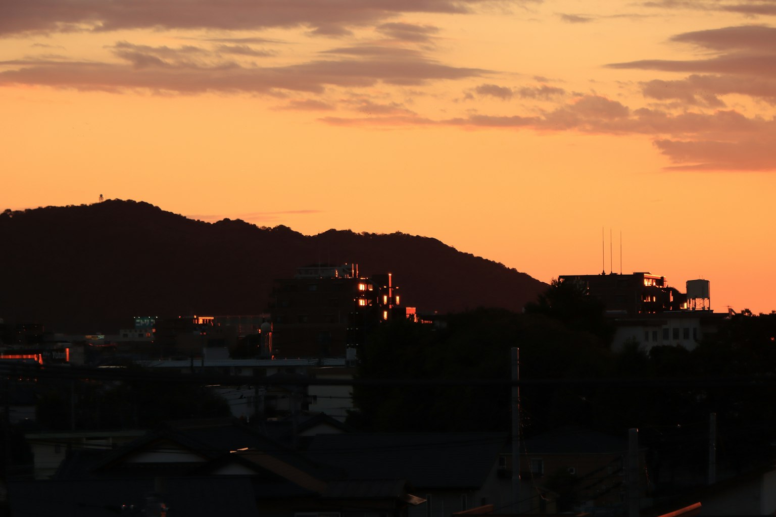 夕焼けの空とシルエットの山々を背景にした都市の風景