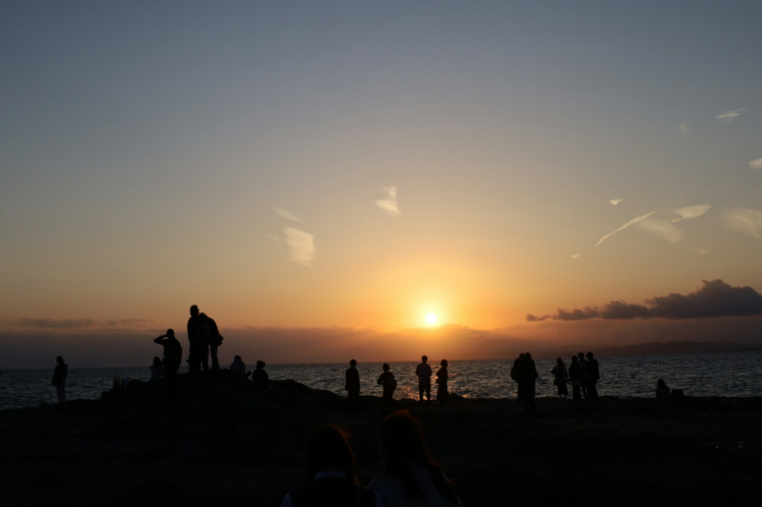 夕日を背景にシルエットの人々が海岸に立っている風景