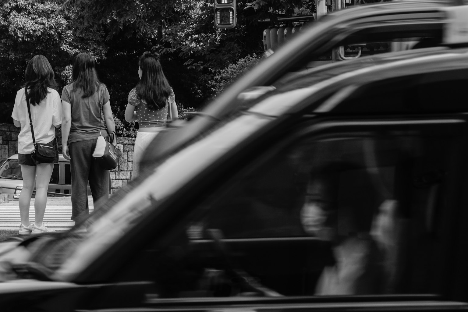 Cảnh đường phố đen trắng với phụ nữ đi bộ trên vỉa hè và xe ô tô đi qua