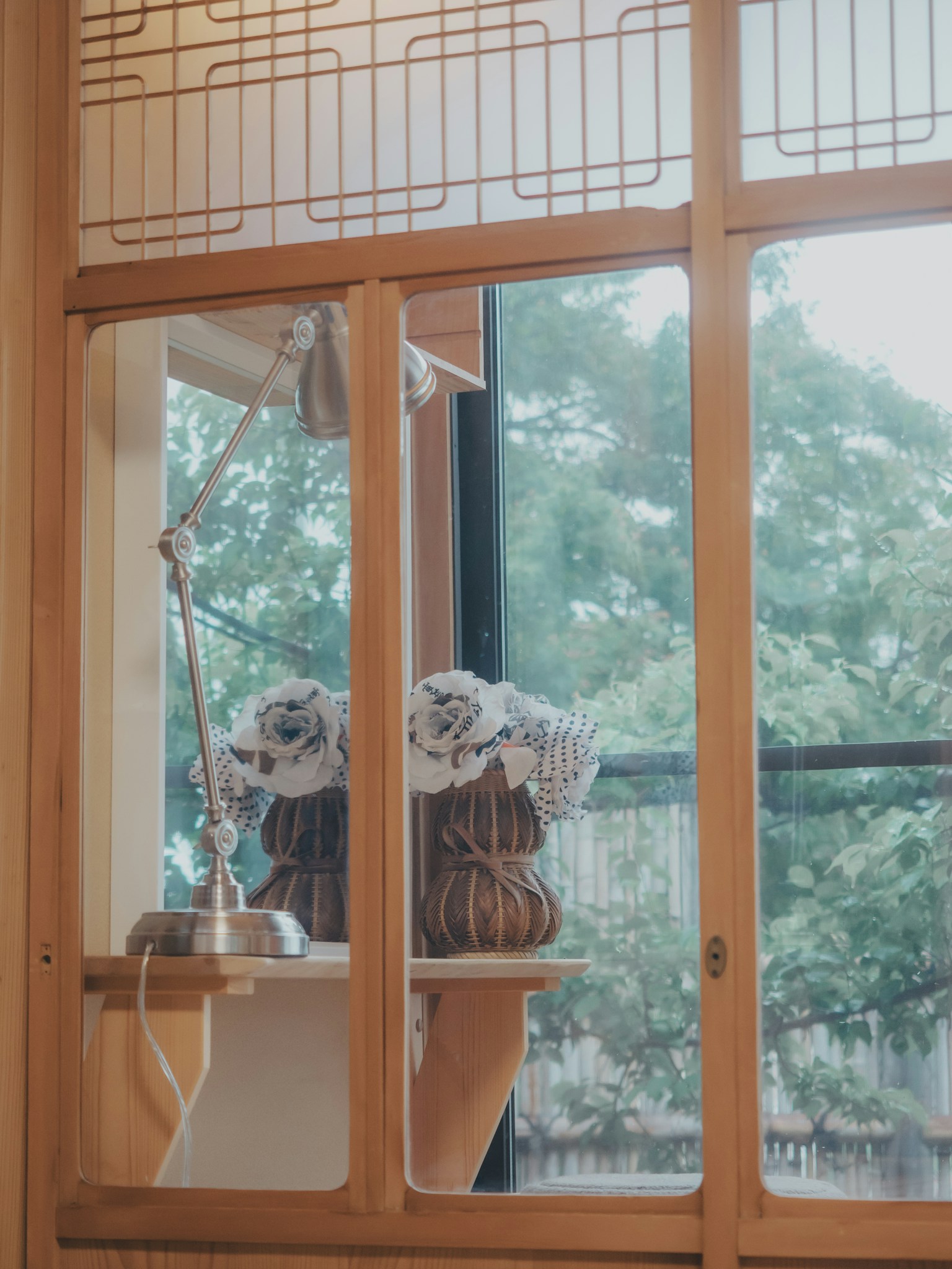 Vista interior a través de una ventana de madera que muestra vegetación y una lámpara elegante