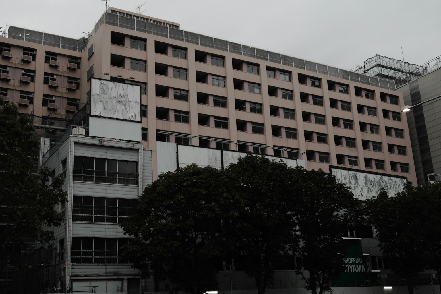 Vista exterior de un edificio bajo nubes grises con paredes rosas y árboles verdes
