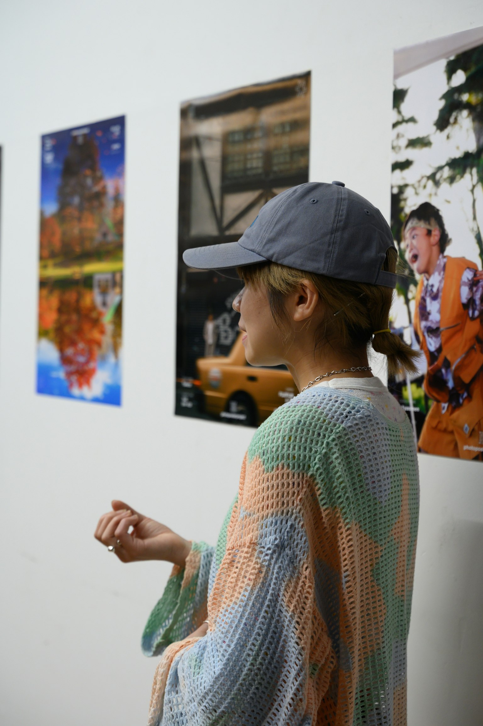 側面看著牆上照片的女性穿著彩色毛衣和帽子