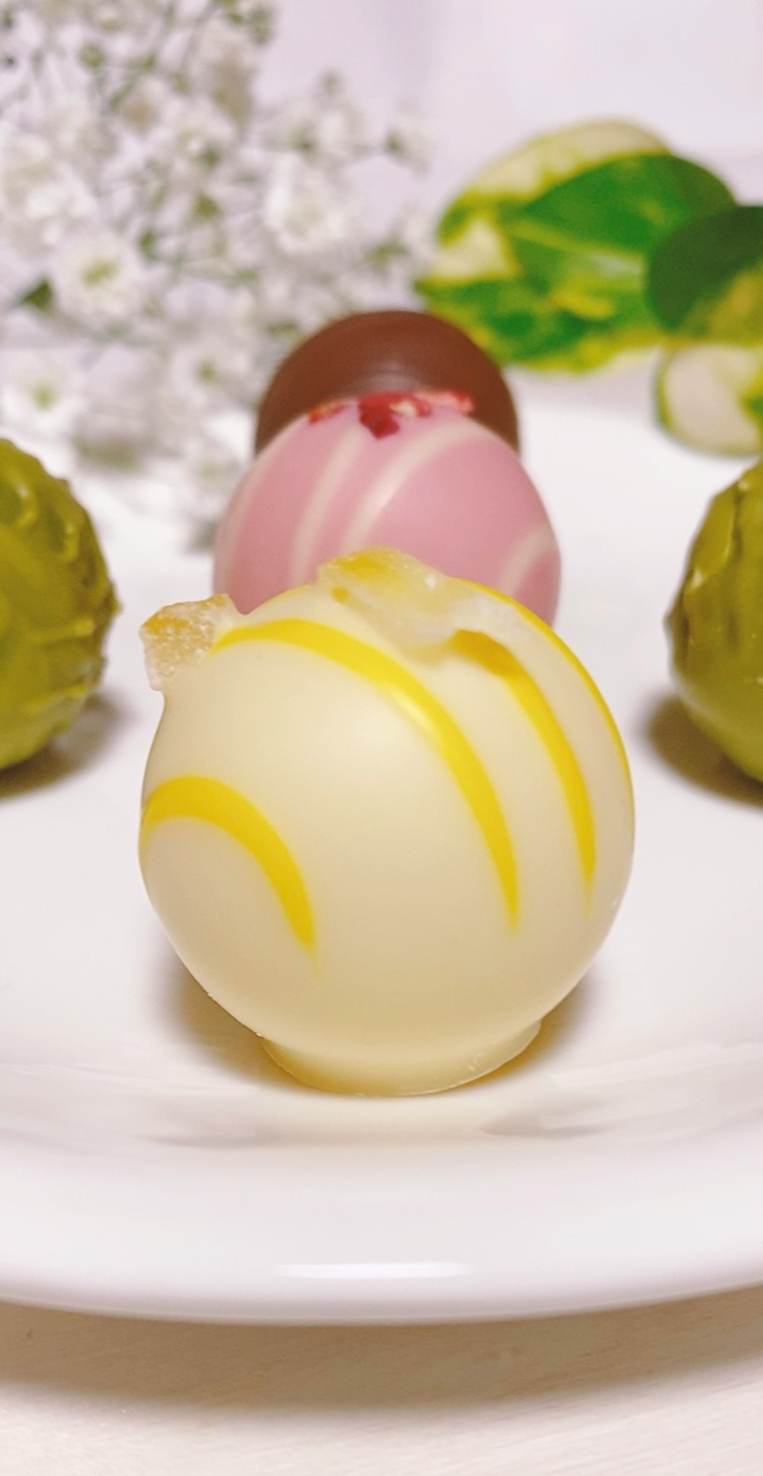 Bola de chocolate blanco con rayas amarillas junto a bolas de chocolate rosa y marrón y bolas verdes en un plato blanco