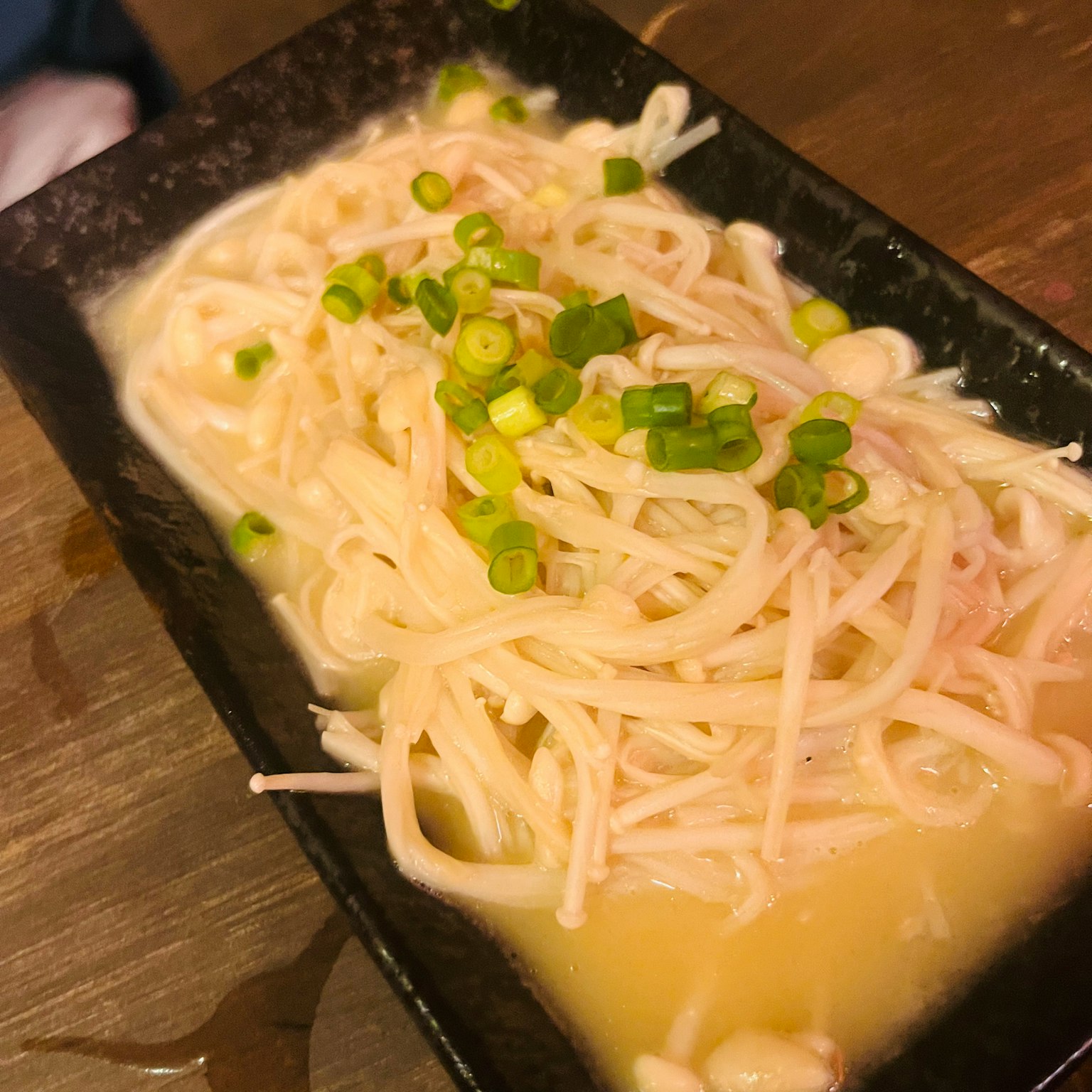 Un piatto di noodles bianchi e carne affettata guarnito con cipollotti verdi