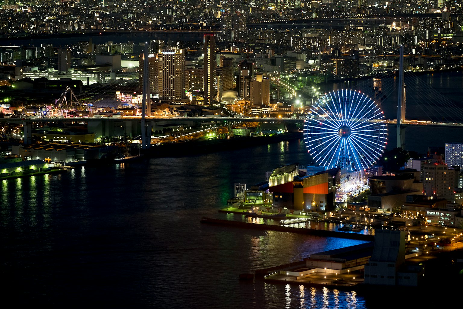 Stadtansicht bei Nacht mit einem beleuchteten Riesenrad und Hafen