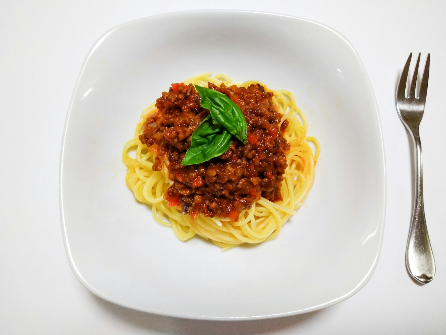 Spaghetti with meat sauce topped with fresh basil on a white plate