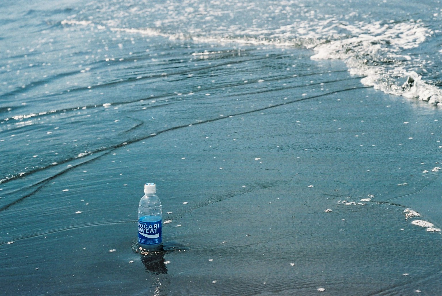 Una bottiglia d'acqua sulla spiaggia con onde che lavano la sabbia