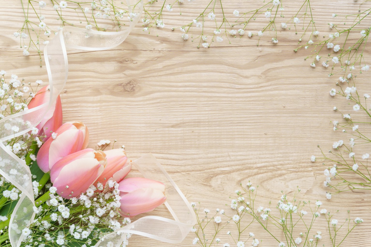 A beautiful bouquet of pink tulips surrounded by baby breath flowers and white ribbon on a wooden table