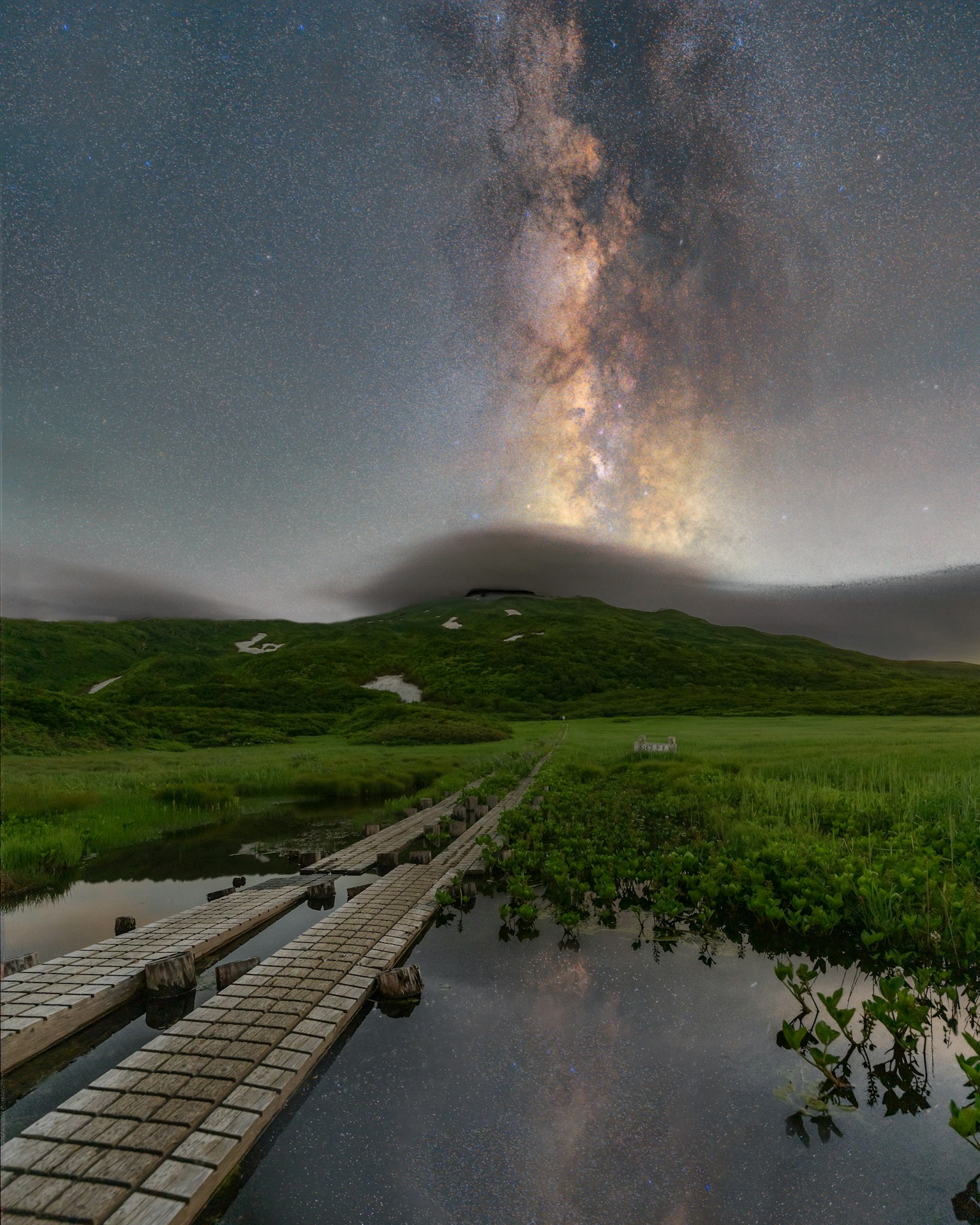 Via Lattea che si estende su un paesaggio sereno con un sentiero in legno e riflessi nell'acqua