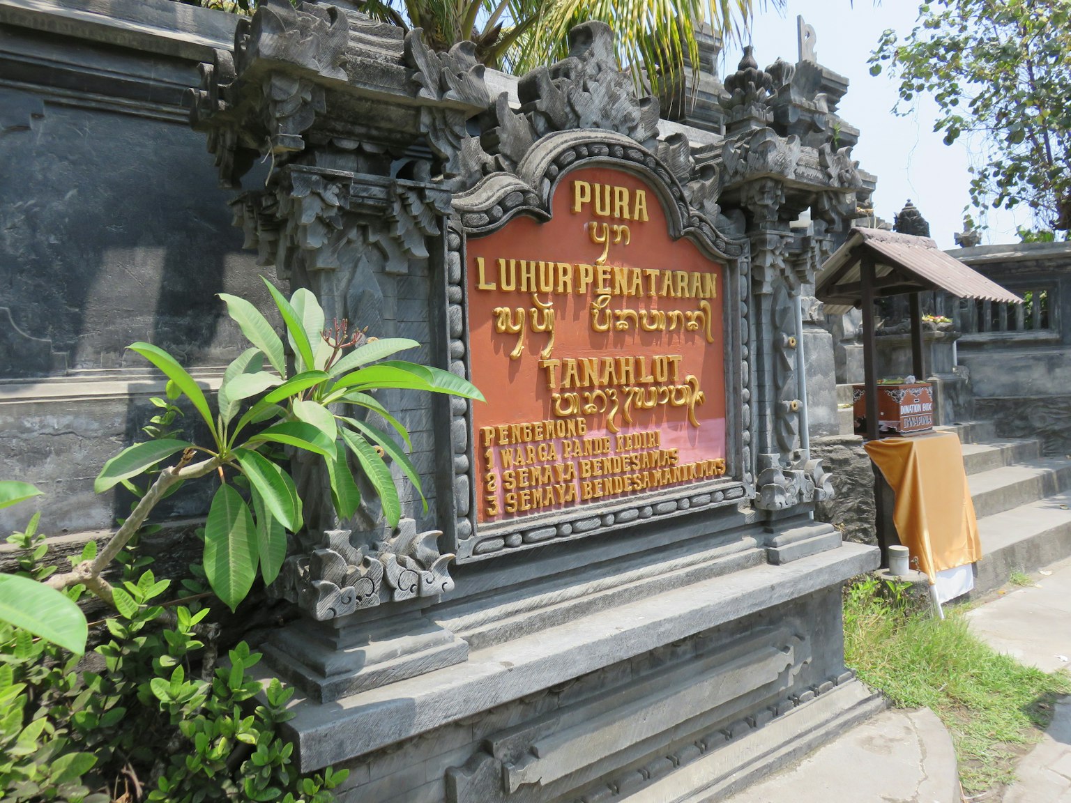 Cartel decorativo de Pura Luhur Pentalan rodeado de vegetación y arquitectura de piedra