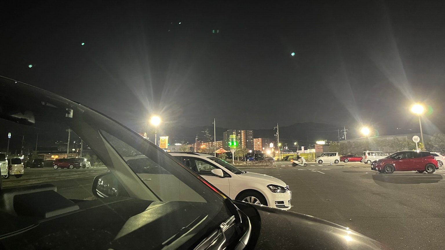 Escena de estacionamiento nocturno con autos negros y blancos iluminados por luces brillantes