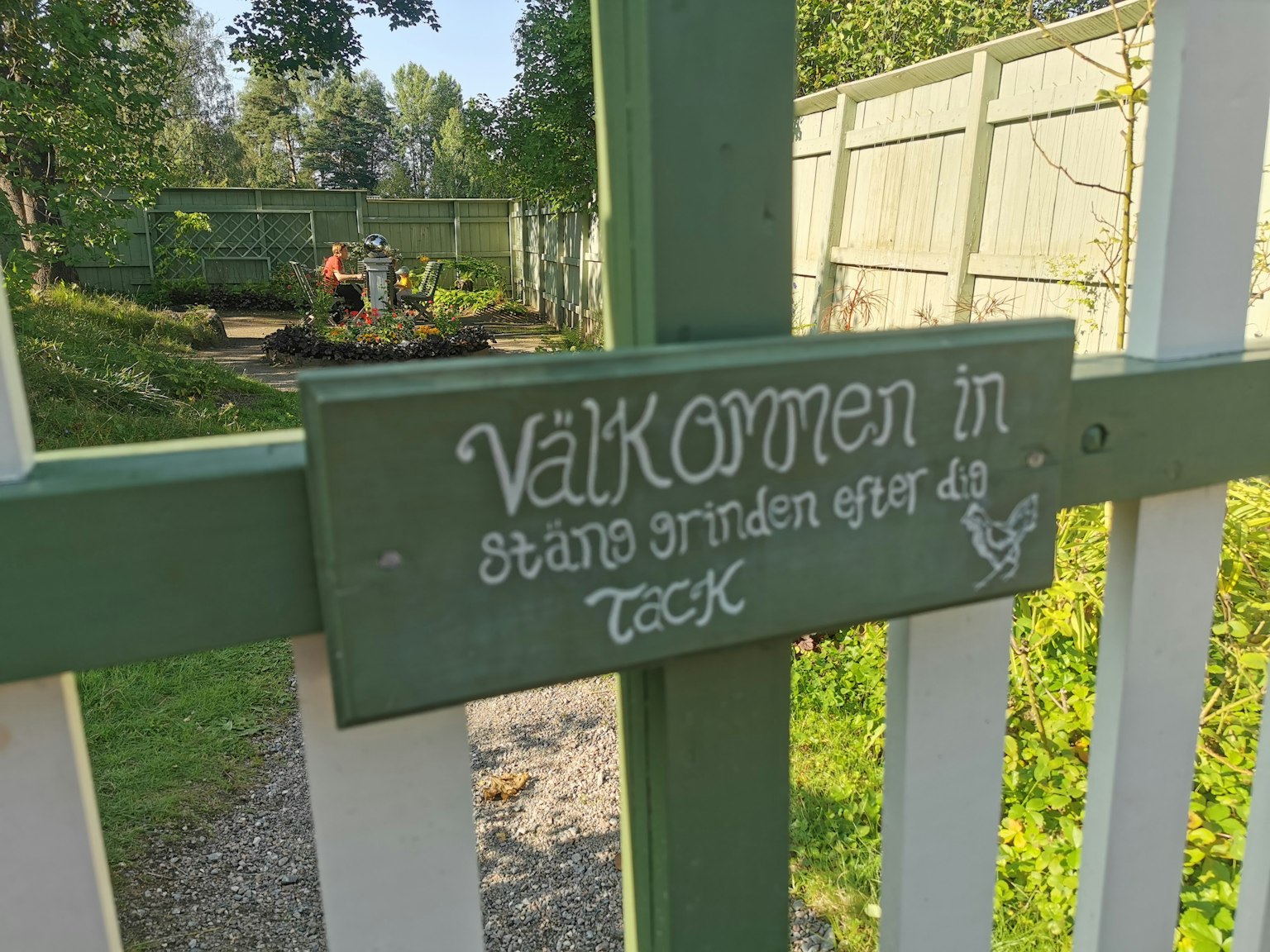 Eingang zu einem Garten mit einem Willkommensschild an einem grünen Zaun