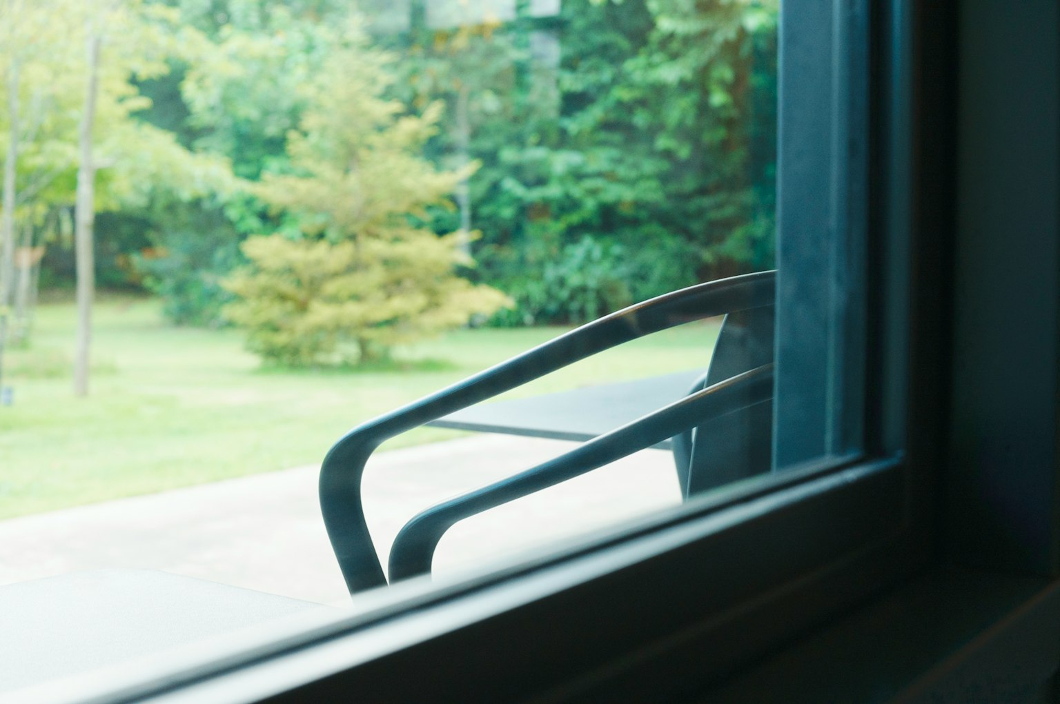 Blick auf einen grünen Garten und einen Teil eines schwarzen Stuhls von einem Fenster aus