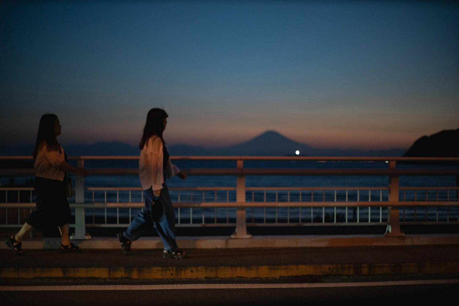 Hai người phụ nữ đi bộ trên cầu vào lúc hoàng hôn với núi Phú Sĩ ở phía sau