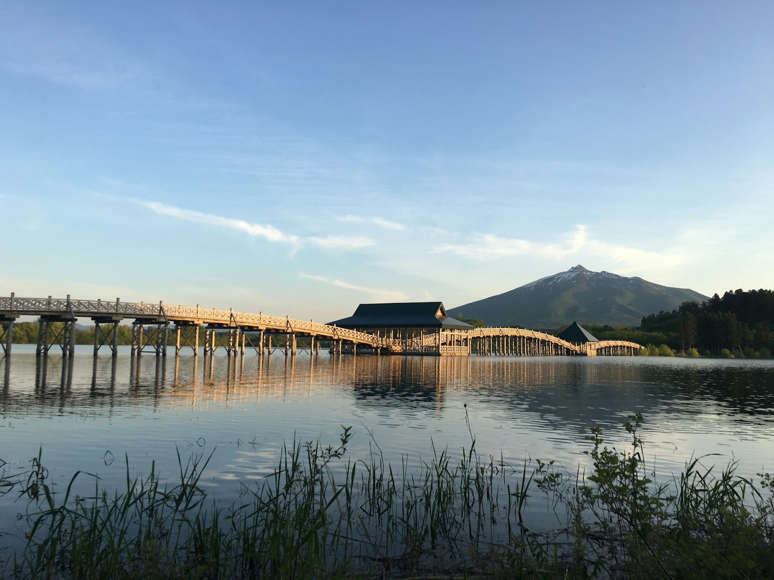 ทิวทัศน์ของสะพานไม้ที่สะท้อนในน้ำพร้อมภูเขาในพื้นหลัง