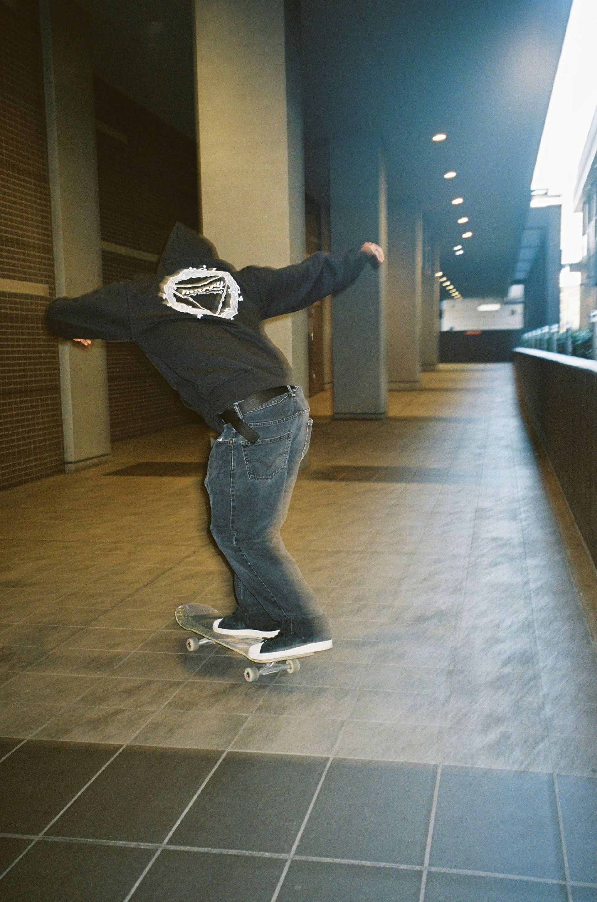 Rückenansicht einer Person beim Skateboardfahren in einem Gebäudegang