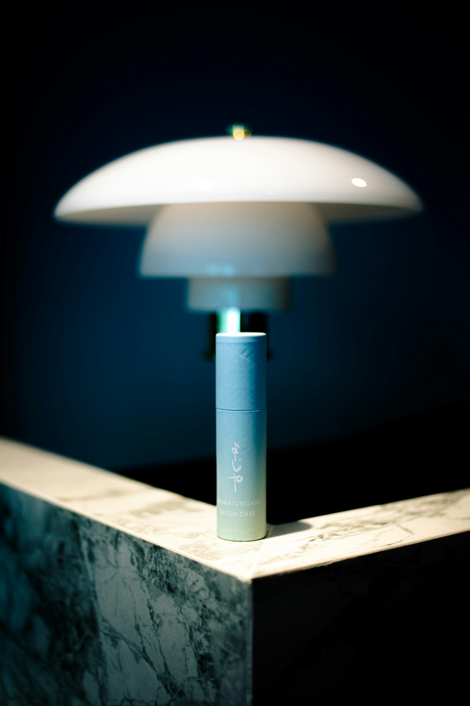 Một chiếc đèn hiện đại với chao trắng phát ra ánh sáng mềm mại trên nền tối