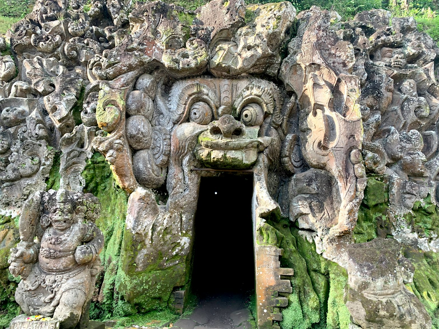 Une entrée de grotte mystérieuse avec des visages sculptés de manière complexe et des sculptures divines environnantes