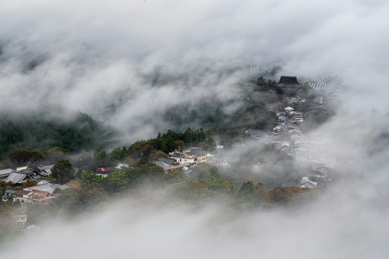 A village nestled in the mountains shrouded in fog houses scattered throughout with a temple-like structure visible