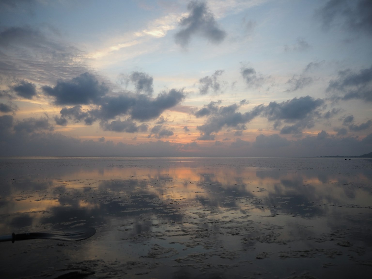 Laut tenang mencerminkan langit dan awan saat matahari terbenam