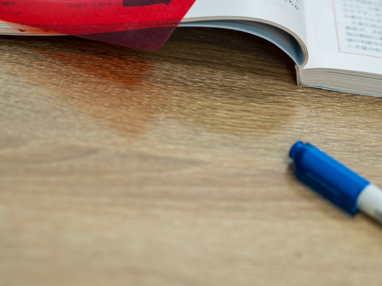 Un libro con copertina rossa e una penna blu appoggiati su un tavolo di legno