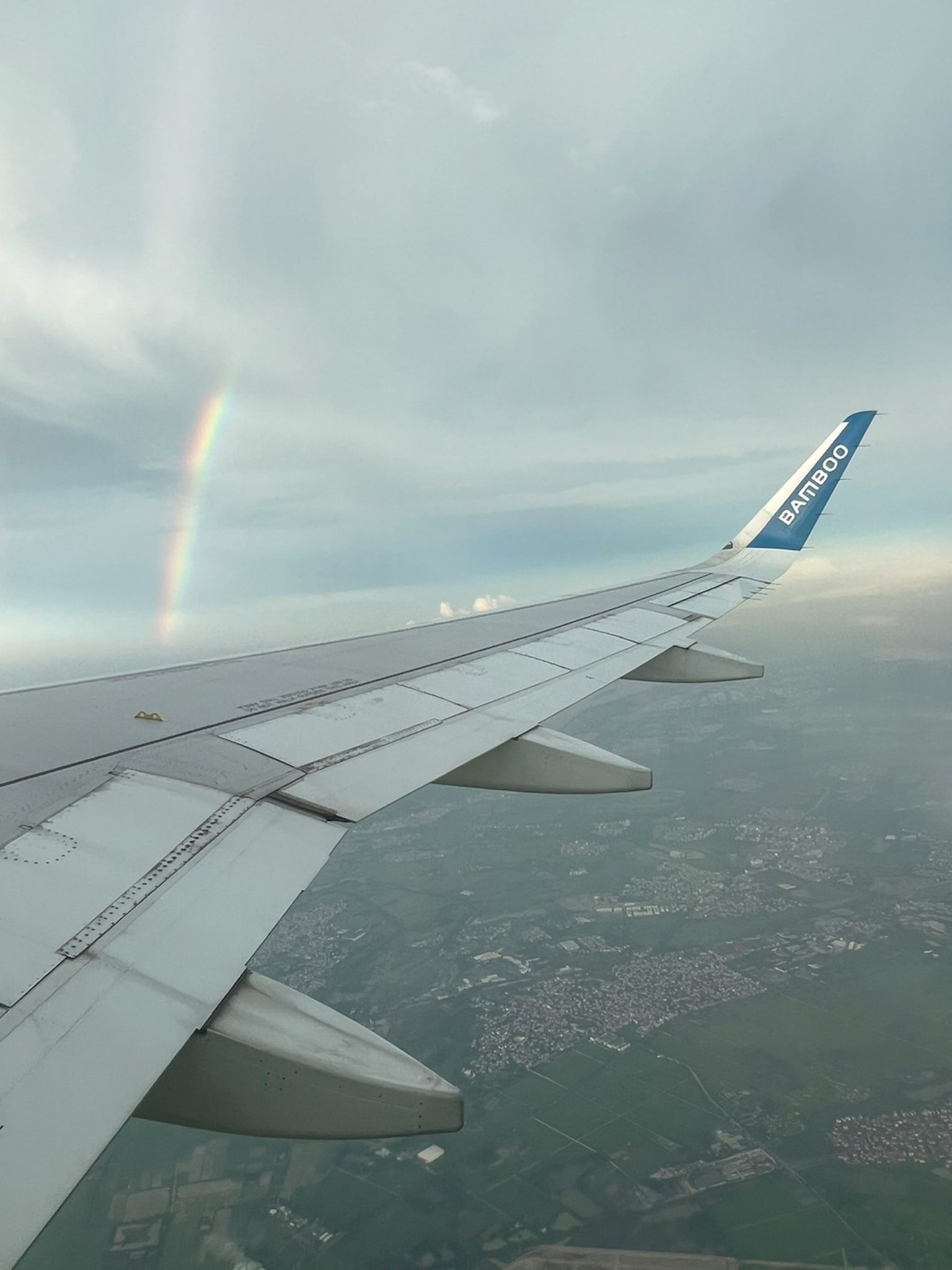 Pemandangan dari sayap pesawat dengan pelangi dan awan