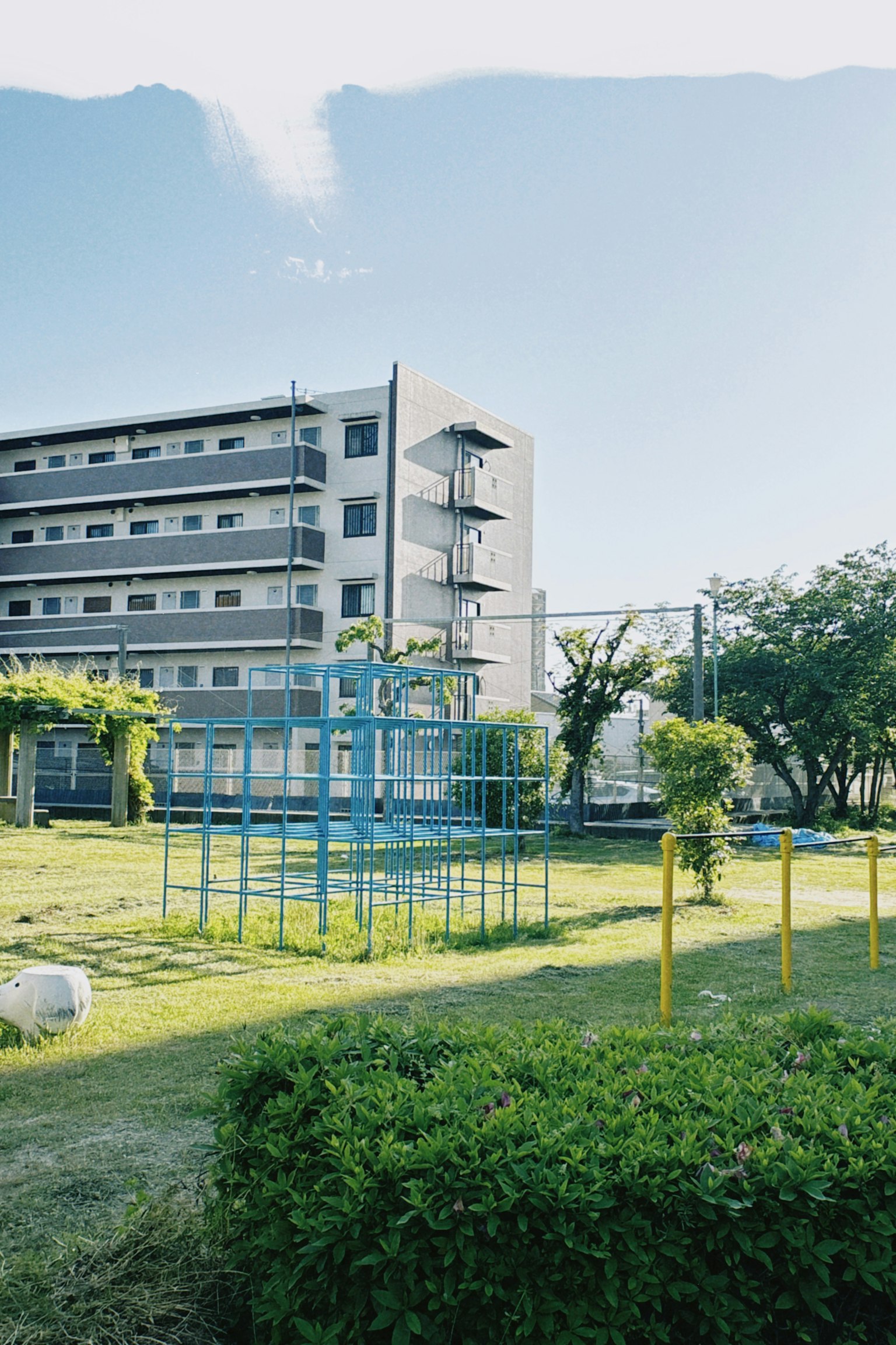 Parkszene mit blauen Spielgeräten und nahegelegenem Gebäude