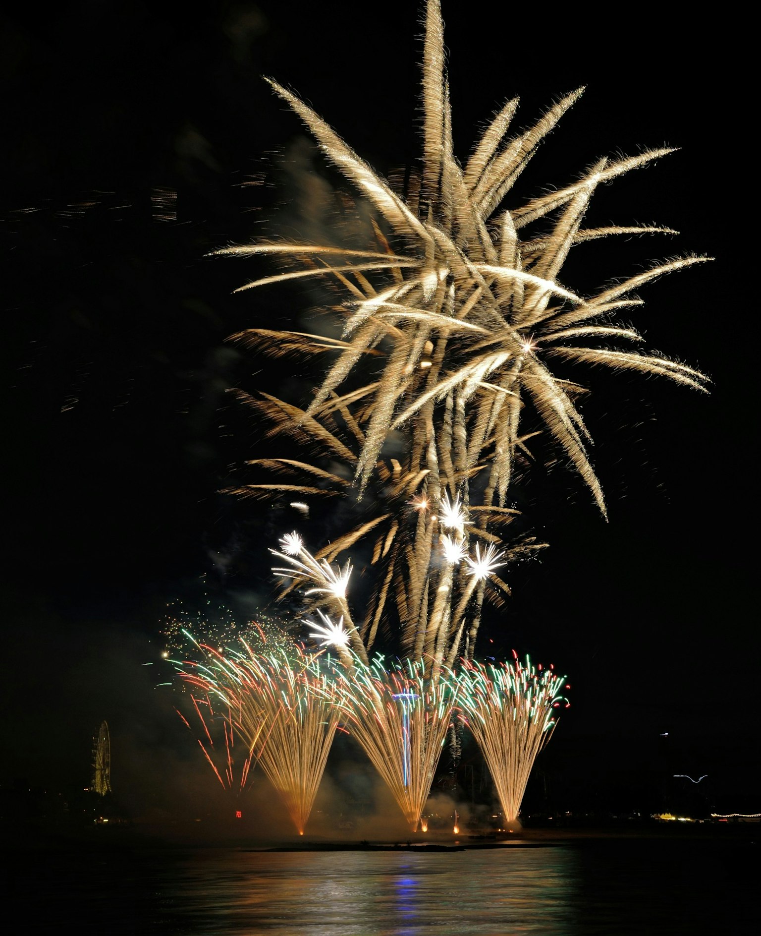 Lebhaftes Feuerwerk, das den Nachthimmel erhellt bunte Funken spiegeln sich im Wasser