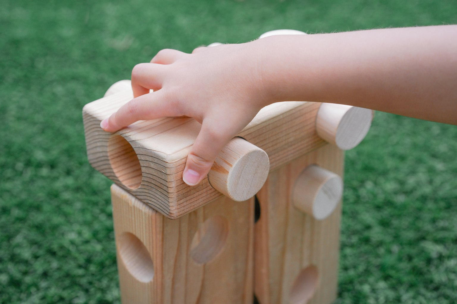 Mano di un bambino che tiene un blocco di legno su un prato verde