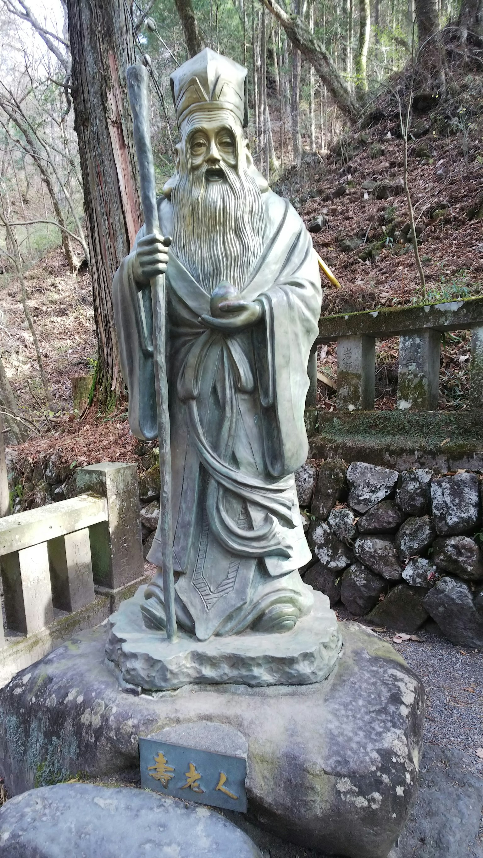 一尊古老的石雕老人手持法杖在森林環境中