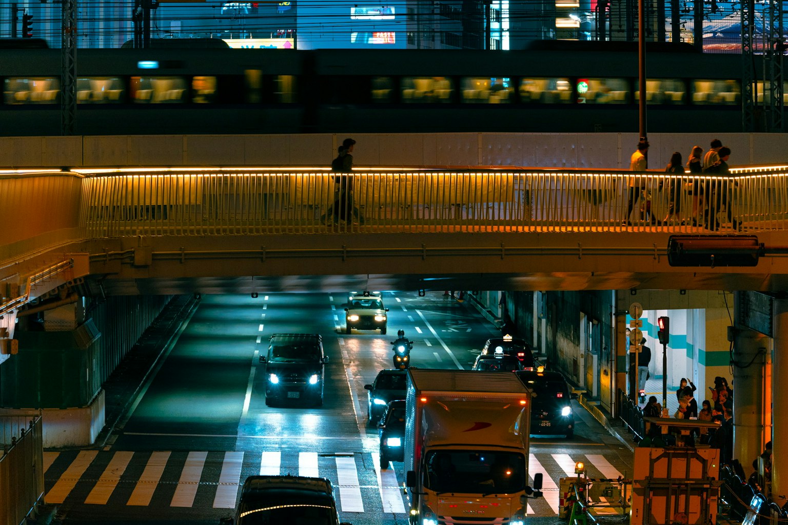 Paesaggio urbano notturno con un ponte pedonale e veicoli sottostanti