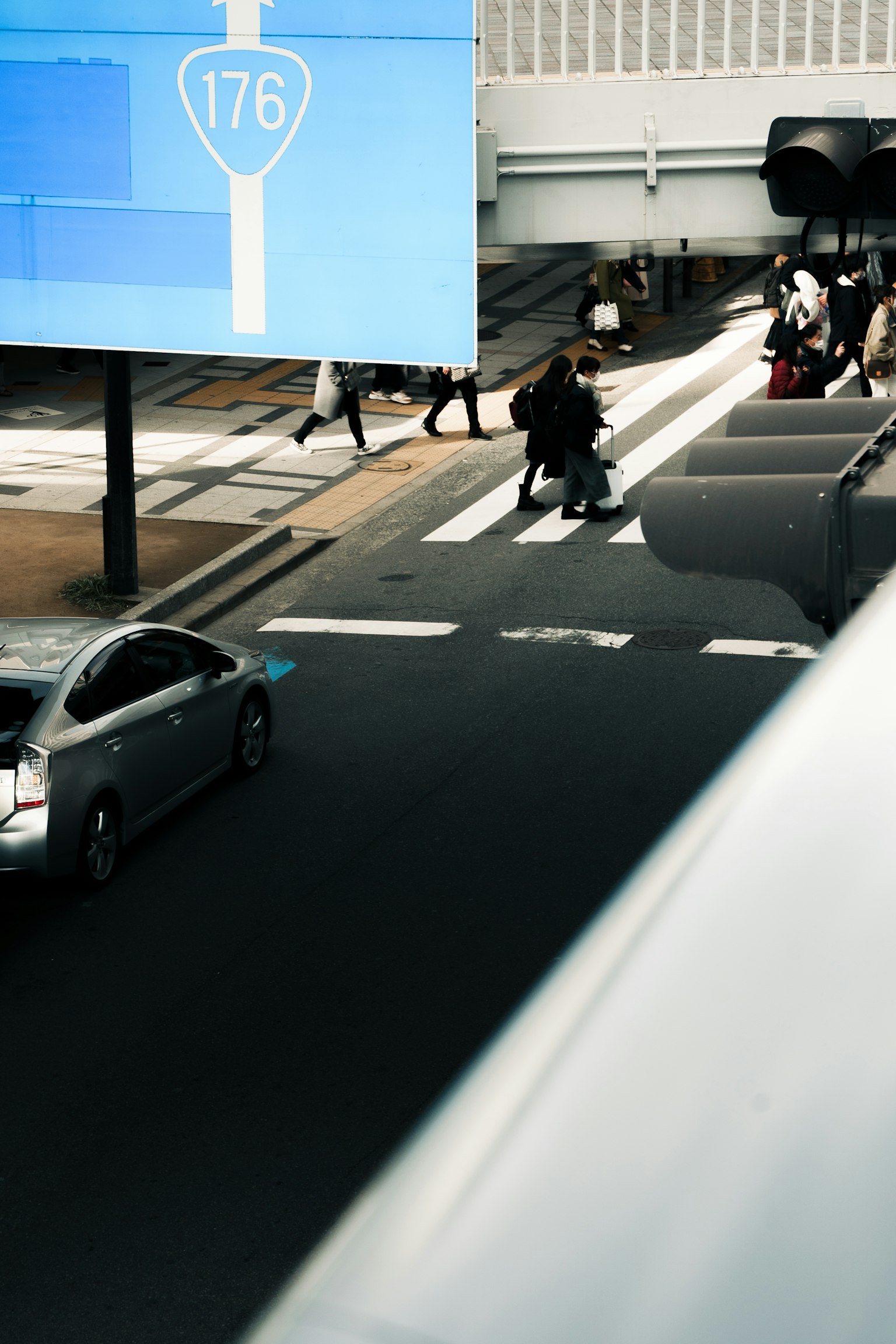 สี่แยกในเมืองที่มีผู้คนเดินอยู่ใต้ป้ายสีน้ำเงินและรถยนต์ที่วิ่งผ่าน
