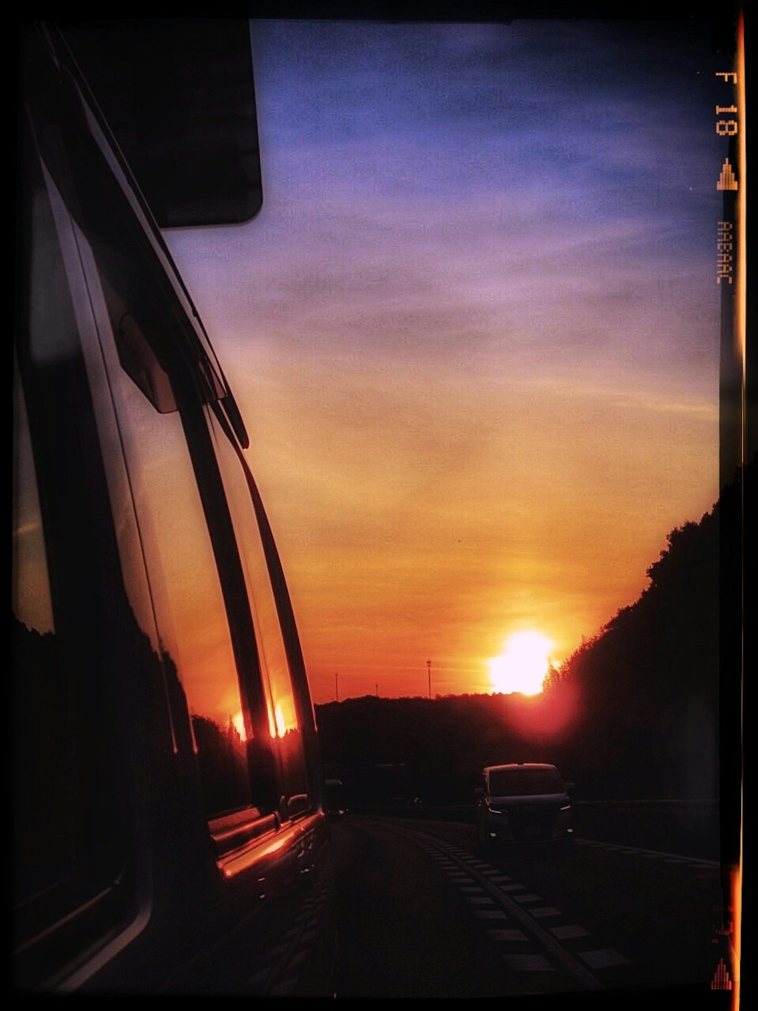 Tramonto riflesso nella finestra di un'auto con una strada panoramica