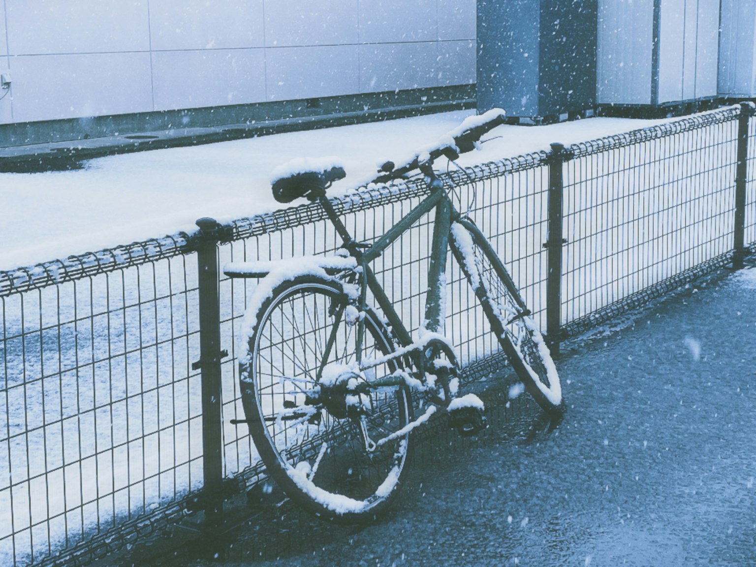 Fahrrad, das im Schnee an einem Zaun lehnt
