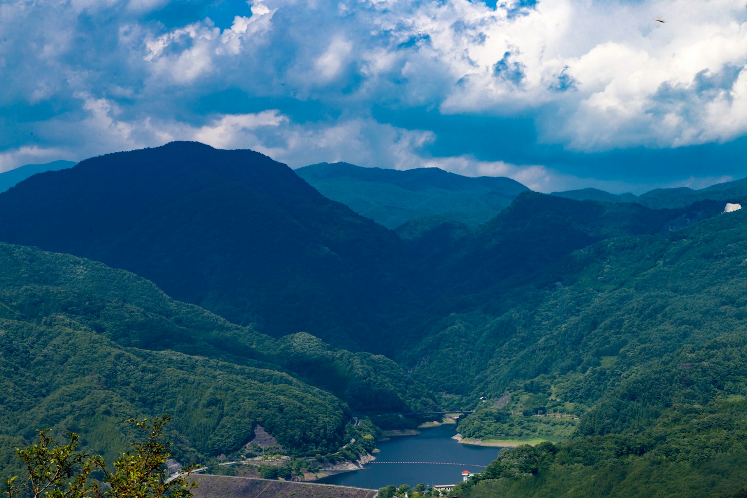 Montañas verdes y un lago sereno bajo un cielo azul con nubes blancas
