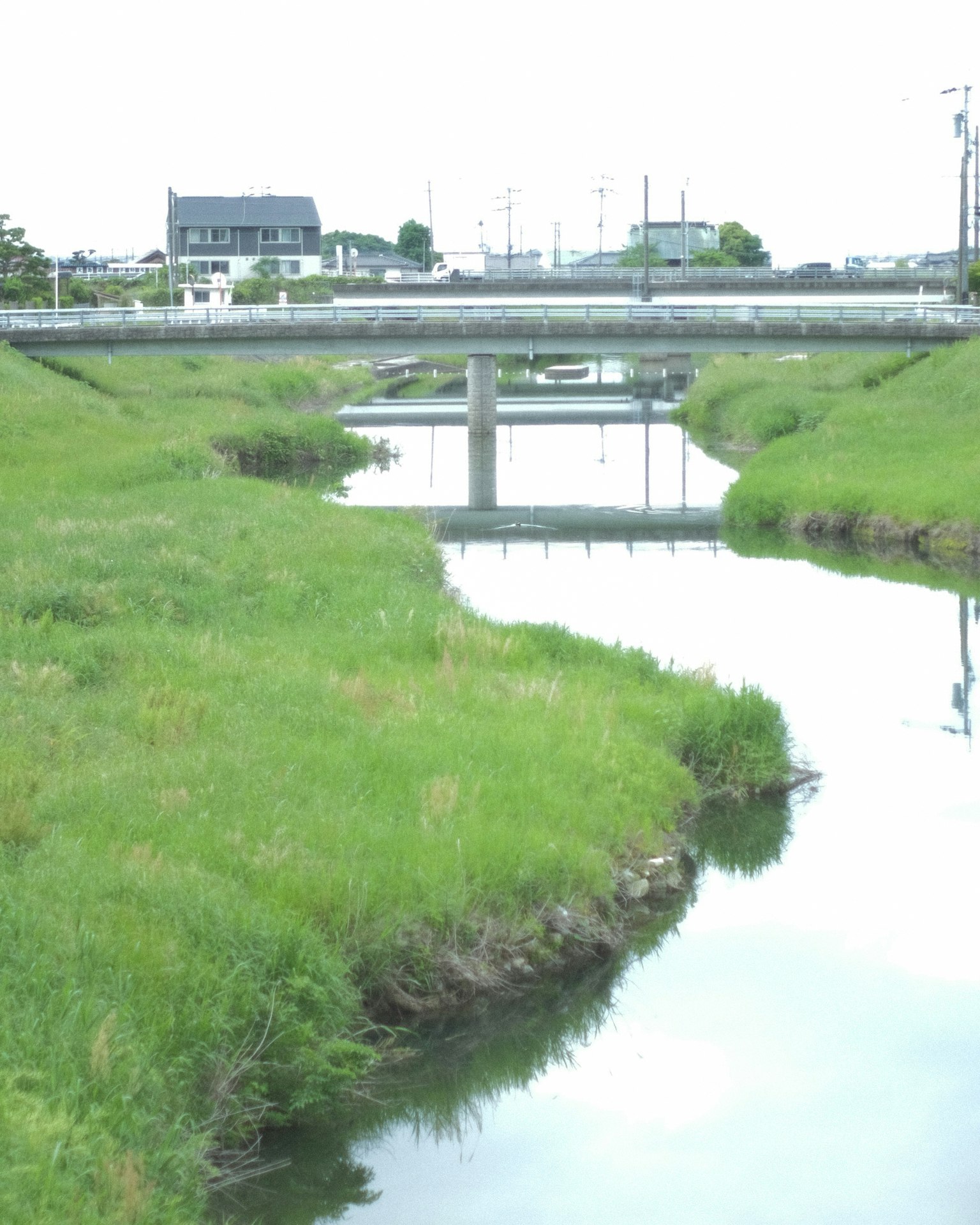 ทิวทัศน์ของสะพานเหนือแม่น้ำสงบล้อมรอบด้วยหญ้าสีเขียว