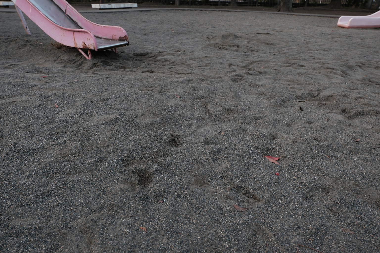 Cầu trượt màu hồng trong khu vực cát của sân chơi với cát xám