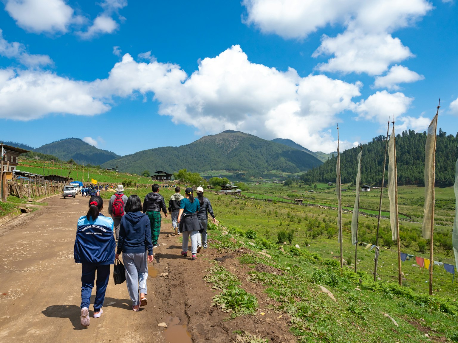 Group of people walking along a rural path with mountains and blue sky
