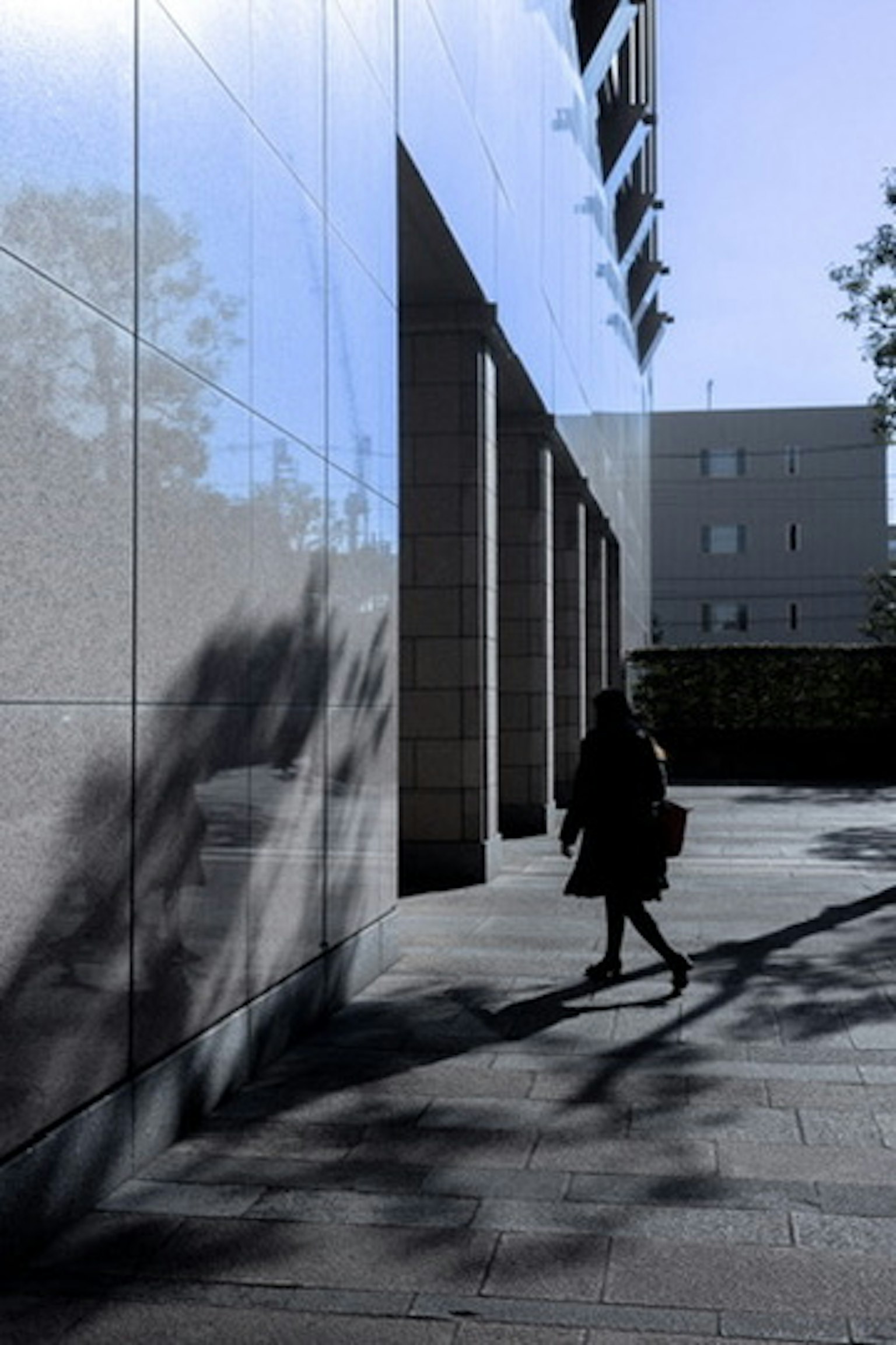 Persona che cammina contro un muro di un edificio moderno che riflette il cielo blu