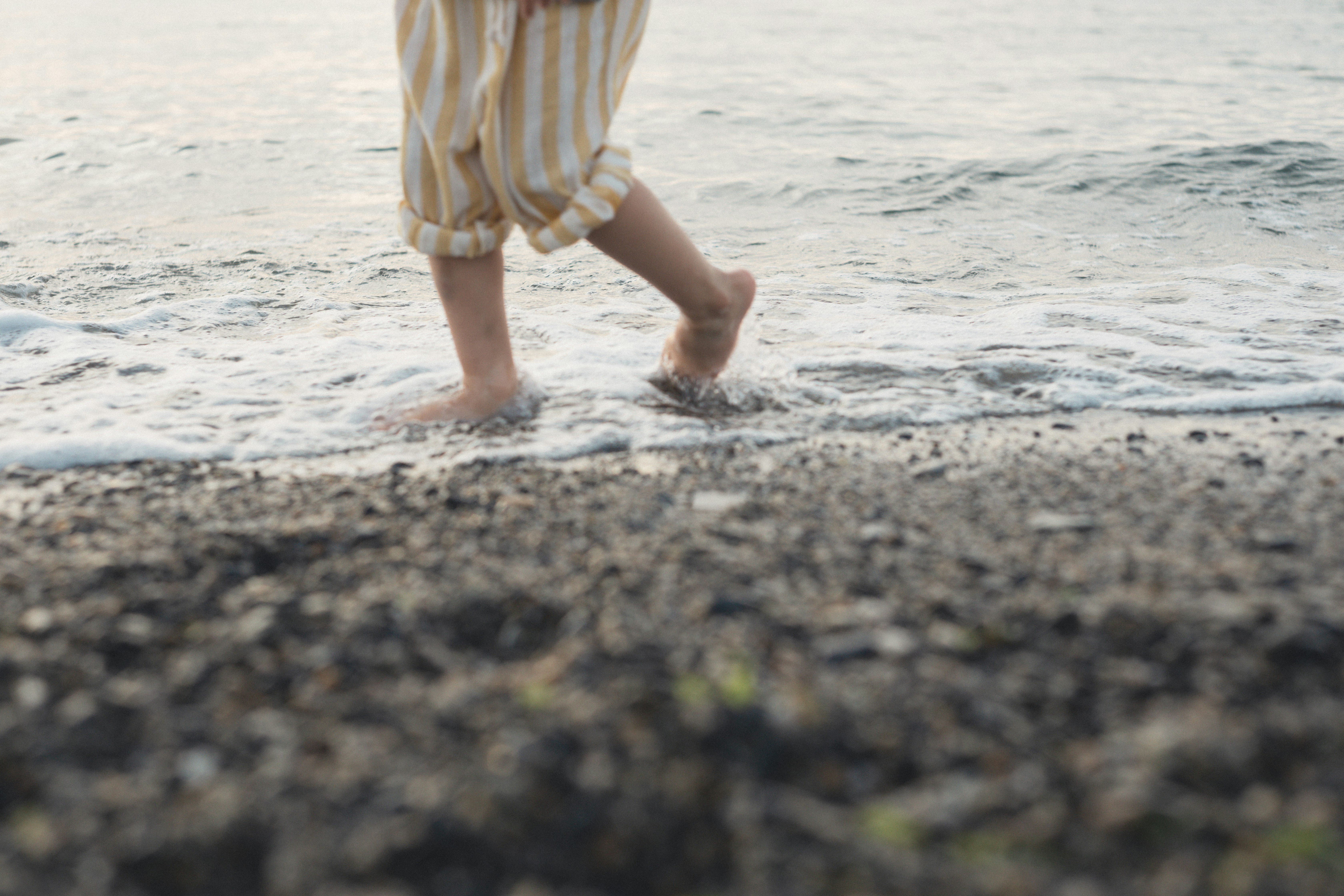 Child's feet in striped pants walking in shallow water at the beach