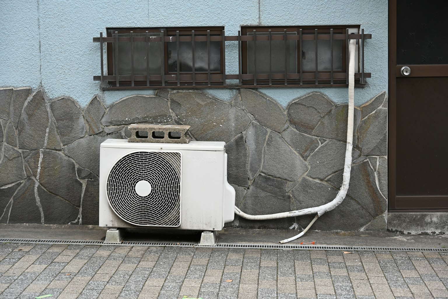 Unità di climatizzazione montata su un muro blu con tubazioni su una superficie di pietra