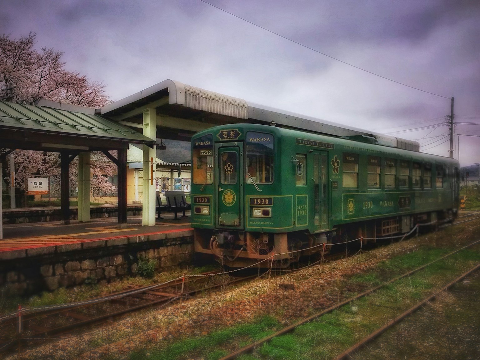 綠色火車停在車站，天空陰雲密布