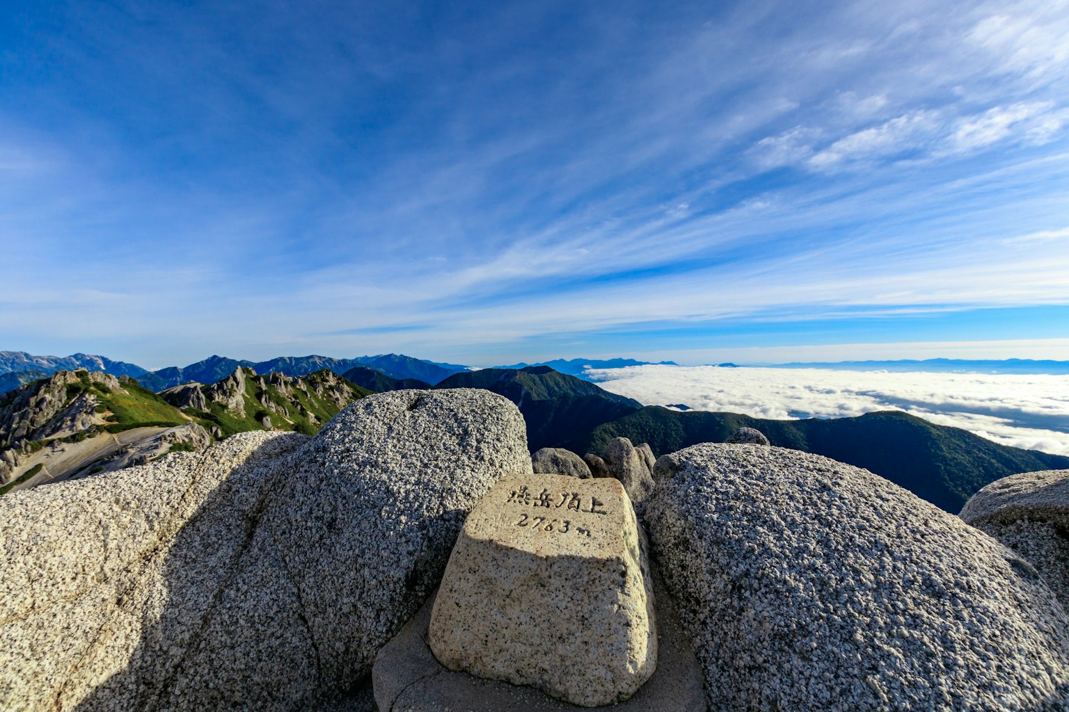Panoramablick auf Berge und Wolkenmeer unter blauem Himmel Fels mit einem Marker